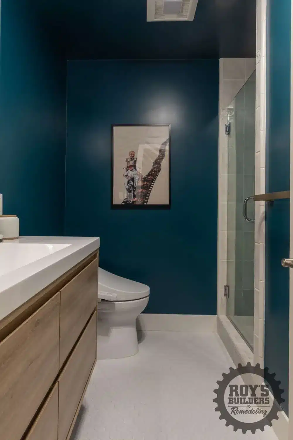 Natural wood vanity with a white countertop and a large gold mirror in a bathroom with dark teal walls