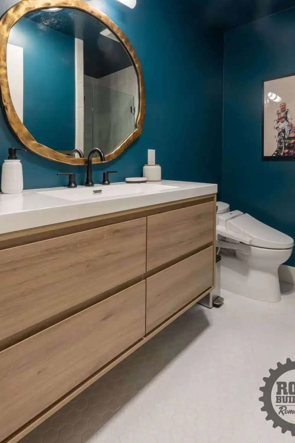 Natural wood vanity with a white countertop and a large gold mirror in a bathroom with dark teal walls