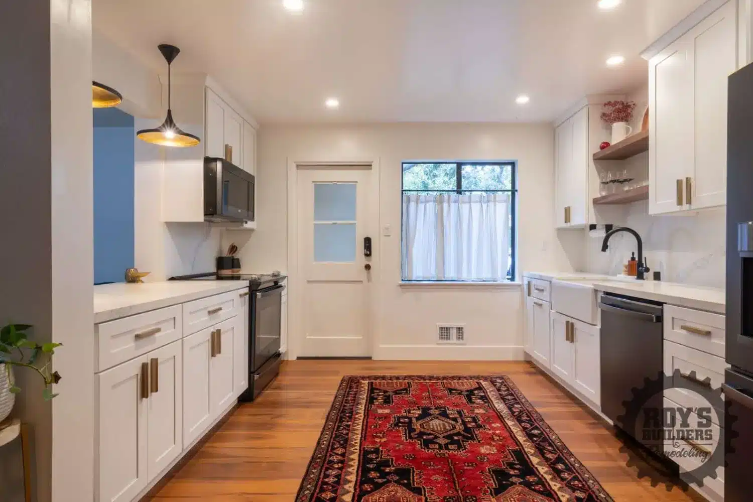 Modern kitchen with white shaker cabinets, a black stove and microwave, a white farmhouse sink, and a red patterned rug on a wood floor