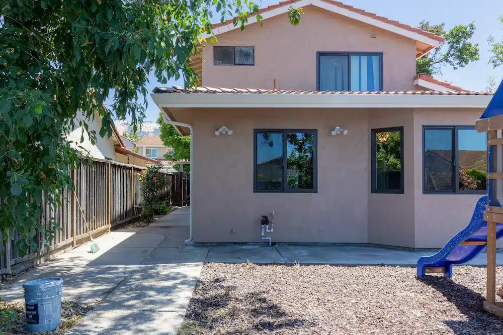 The side of a two-story beige stucco house with a concrete path and blue slide.