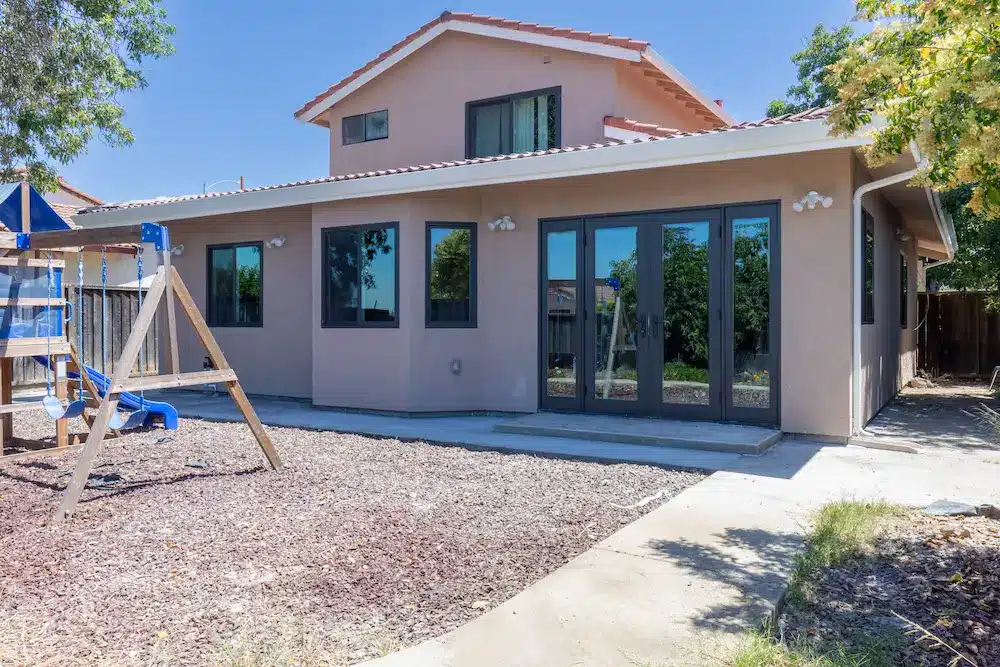 The side of a two-story beige stucco house with a concrete path and blue slide.