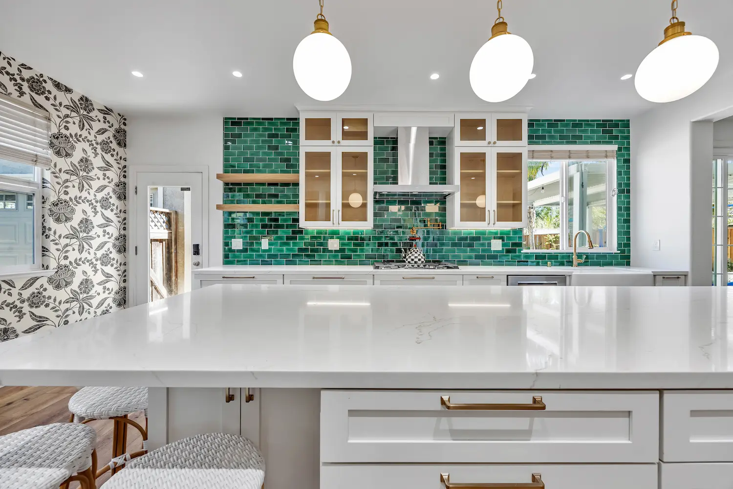 Wide-angle shot of the entire kitchen including the island, green backsplash, and globe pendants.