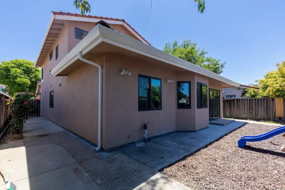 The side of a two-story beige stucco house with a concrete path and blue slide.