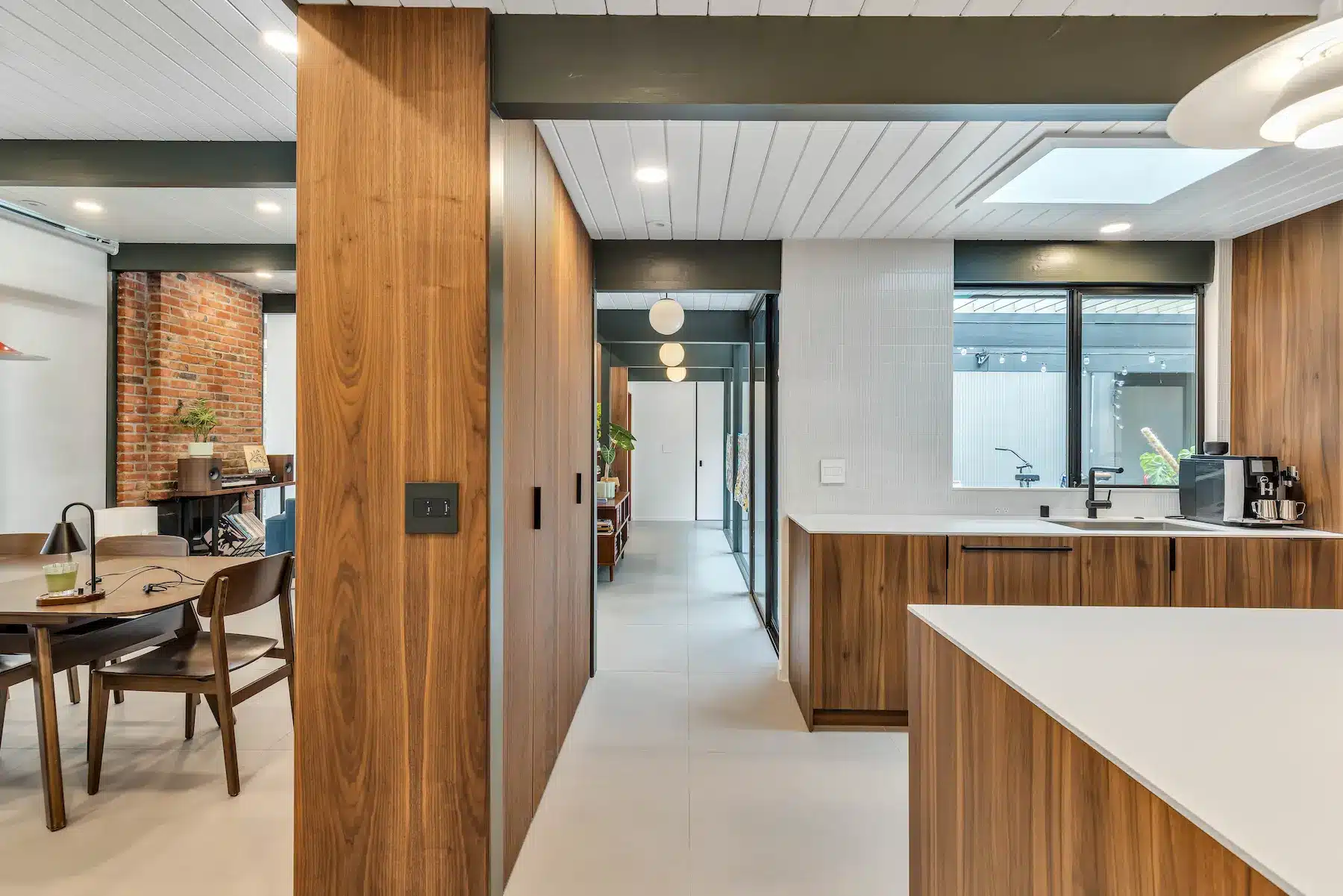 A perspective shot of a hallway lined with wood panels leading past a kitchen towards a dining table.