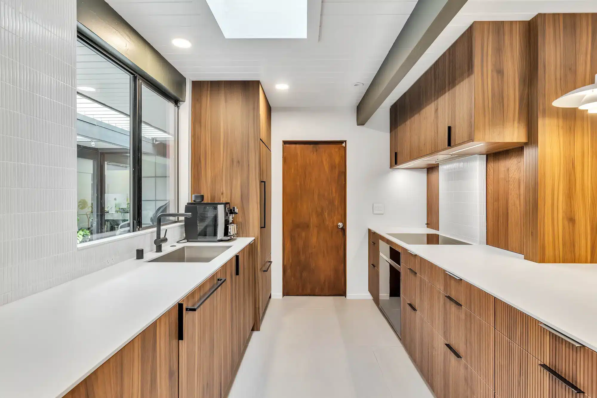 A long galley-style kitchen with wood cabinets on both sides and bright white counters.