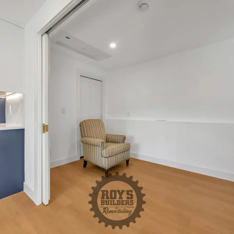 An empty room with light wood floors, white walls, and a single armchair.