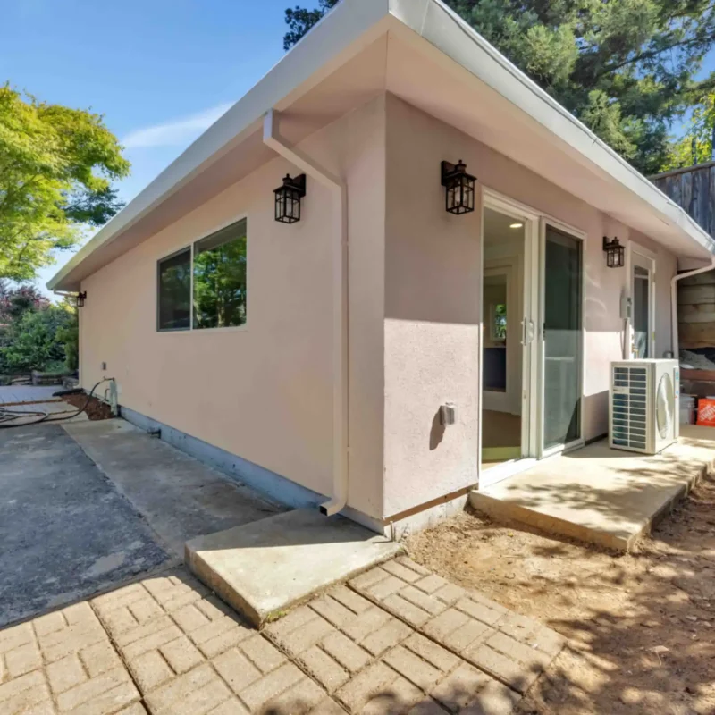 Back exterior view of the house highlighting a sliding glass door and concrete patio walkway.