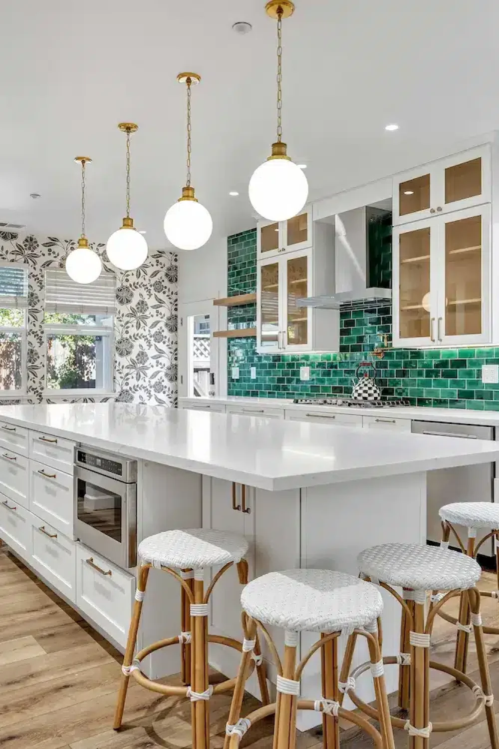 An airy kitchen with white cabinetry, a large white island with gold-trimmed stools, and a vibrant emerald green tiled backsplash.