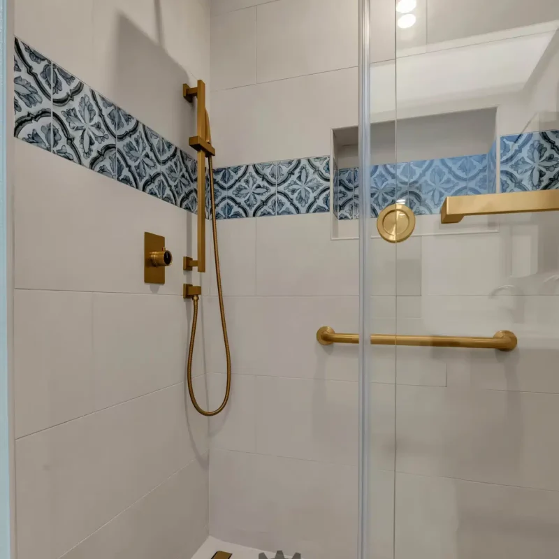 Clean shower stall with white vertical tiling, a gold shower head, and a gold grab bar.