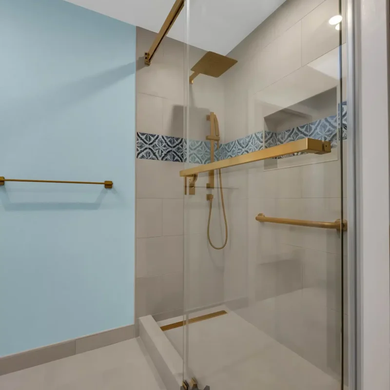 Close-up view of a walk-in shower with a glass sliding door and a blue tile accent line.