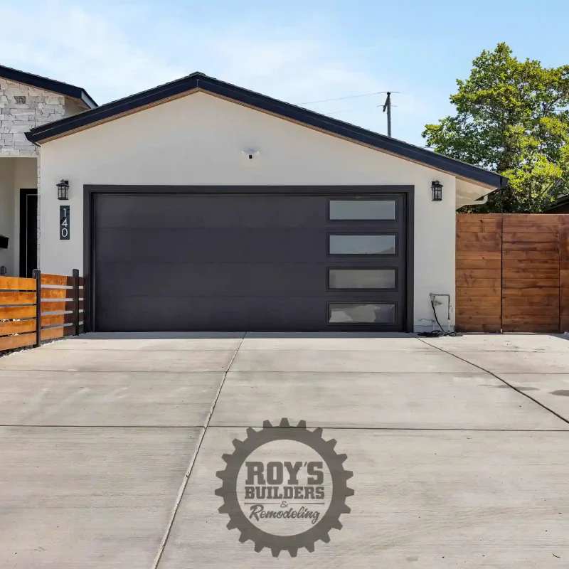 Front yard courtyard featuring a modern black garage door and paved driveway.