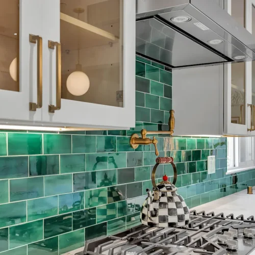Close-up of glossy green subway tiles behind a professional gas range stove.