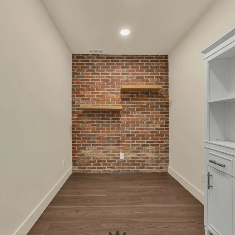 Empty room featuring a rustic red brick accent wall with floating wooden shelves.