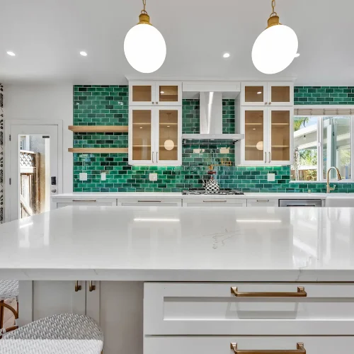 Wide-angle shot of the entire kitchen including the island, green backsplash, and globe pendants.