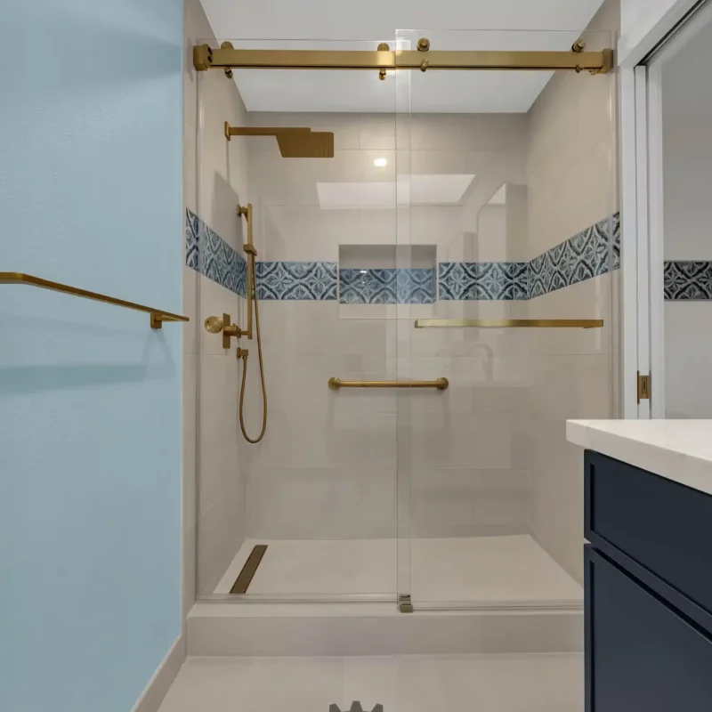Glass-enclosed walk-in shower featuring a blue accent tile trim and gold accents.