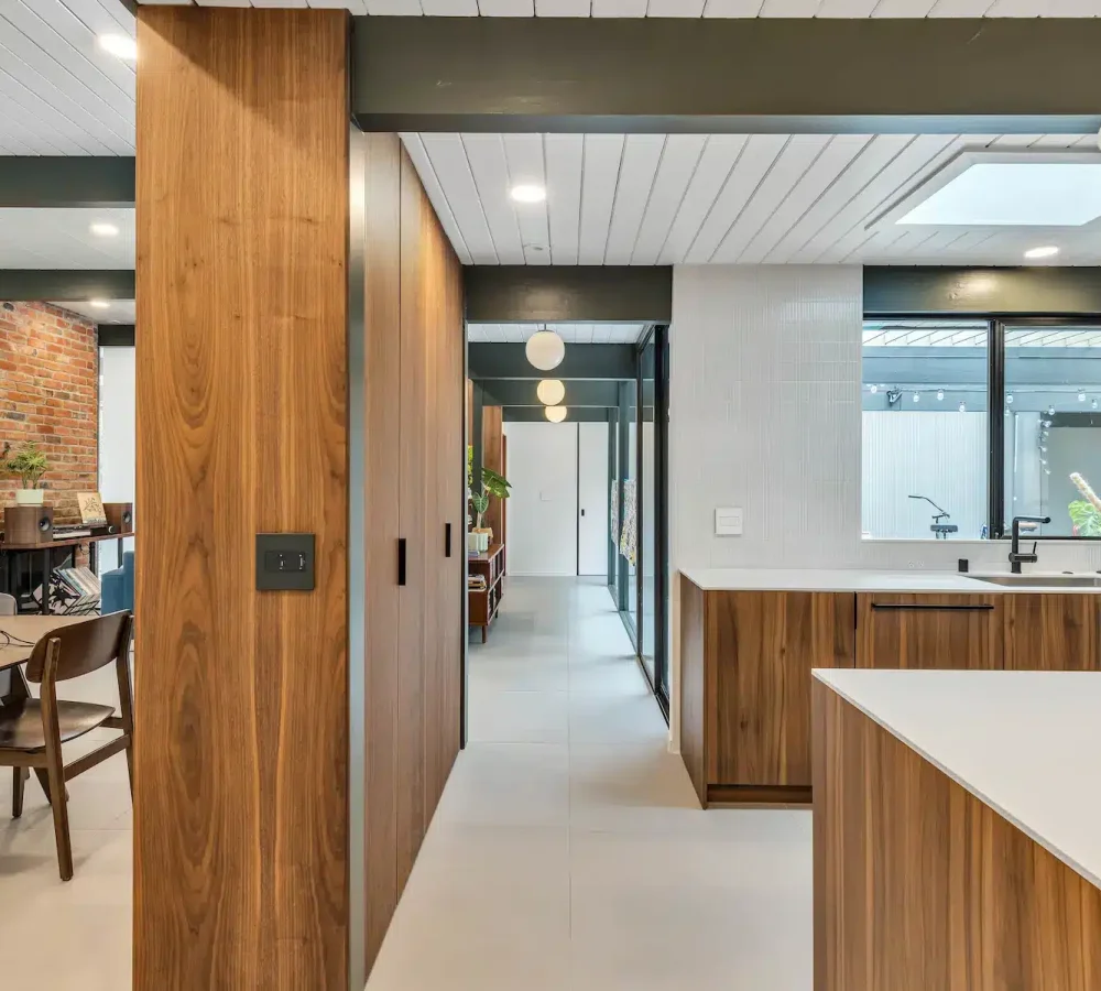 A perspective shot of a hallway lined with wood panels leading past a kitchen towards a dining table.
