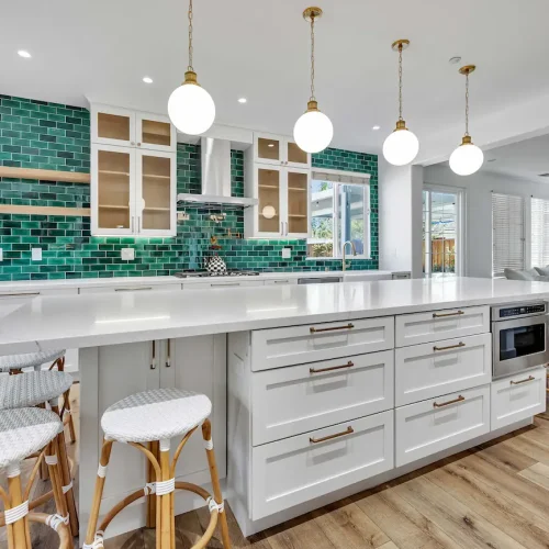 Angled view of a large white kitchen island with white barstools and hanging globe lights.