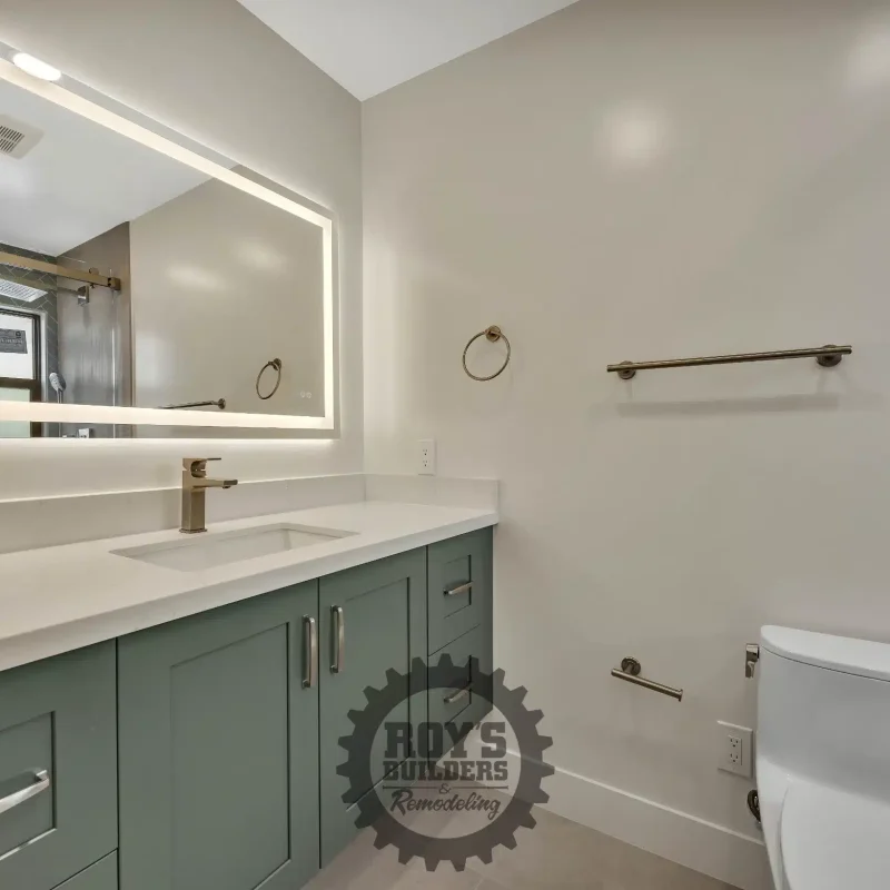 Modern bathroom vanity featuring a green accent wall and illuminated mirror.