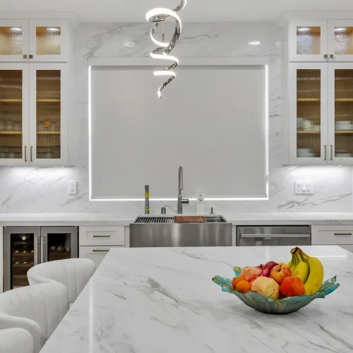 Frontal view of a white marble kitchen island with a bowl of fruit and glass-front cabinets.