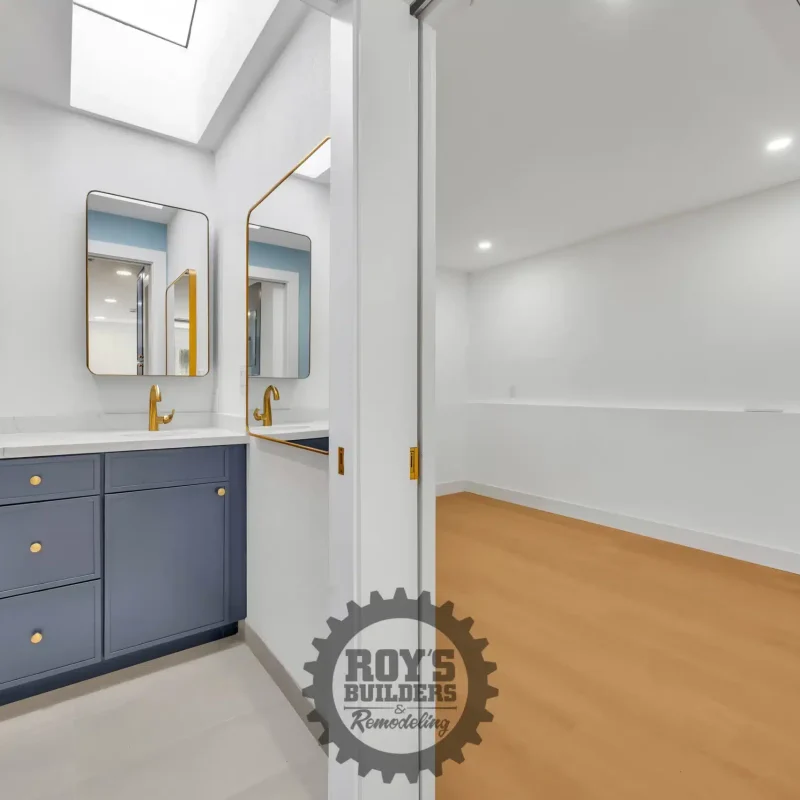 Modern bathroom with a long blue vanity, double gold-rimmed mirrors, and white walls.
