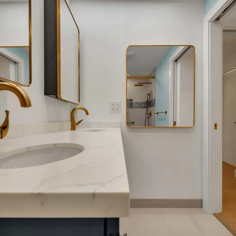 Modern single-sink vanity with white marble look countertop and a gold faucet.