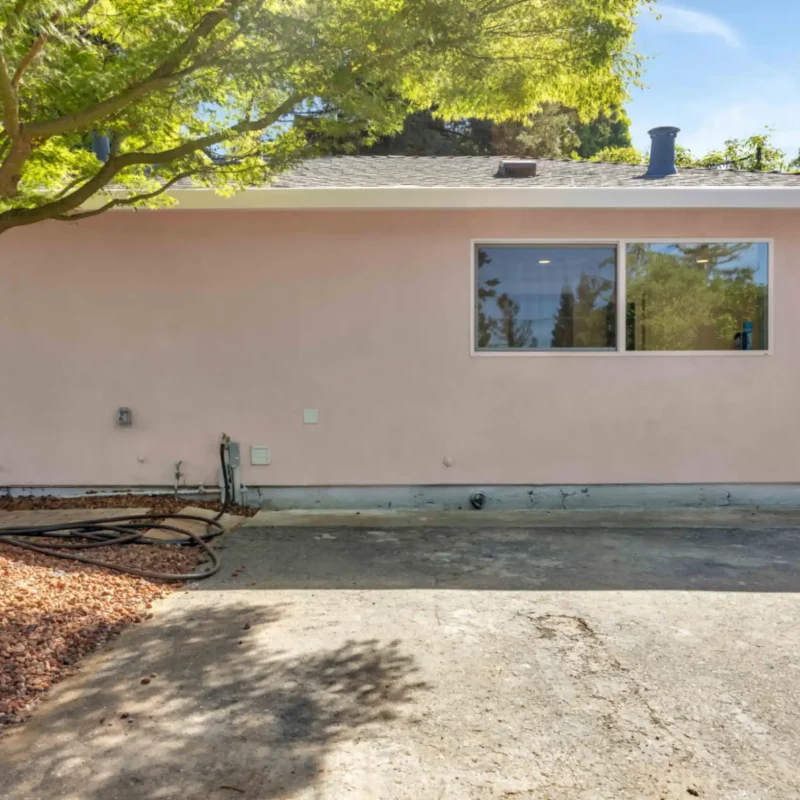 Side exterior of the light-pink building showing a wide window and gravel driveway.