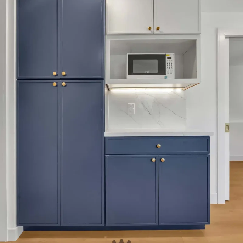 Tall blue pantry cabinet built into a kitchen wall next to an upper microwave shelf.