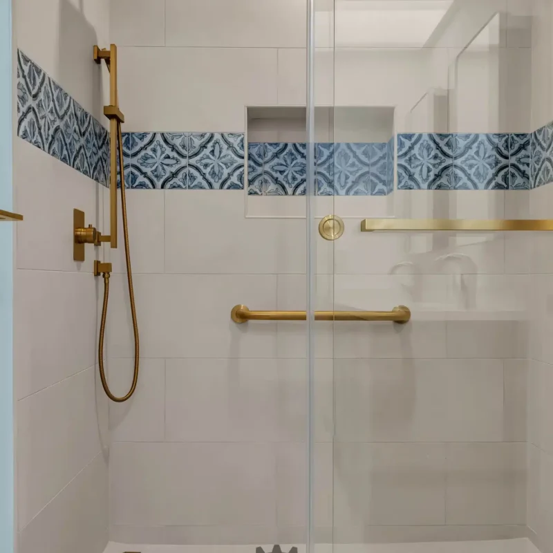 Straight-on view of a modern walk-in shower with gold hardware and white tiling.
