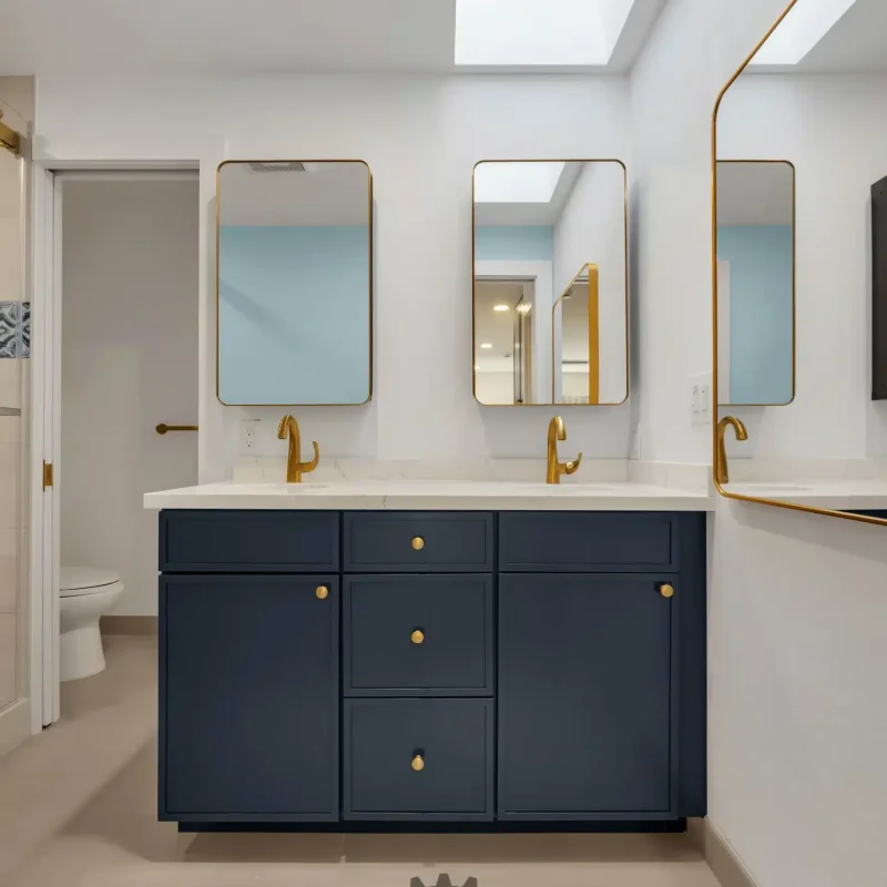 Vertical shot of a bathroom vanity with blue cabinets and gold fixtures under a skylight.