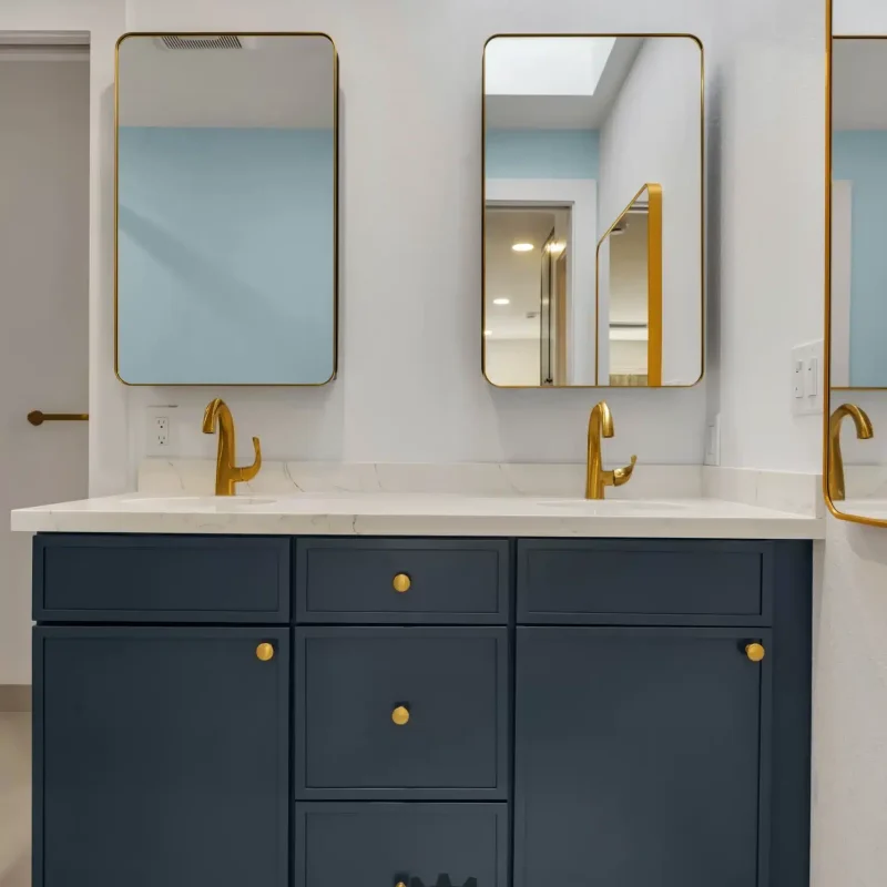 Front-facing view of a double-sink blue vanity with elegant gold hardware and rectangular mirrors.
