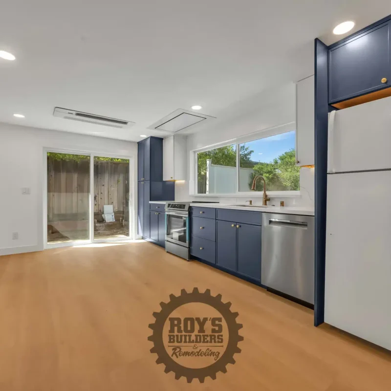 Angled perspective of the modern kitchen layout showing the refrigerator, blue cabinetry, and the bright main room.