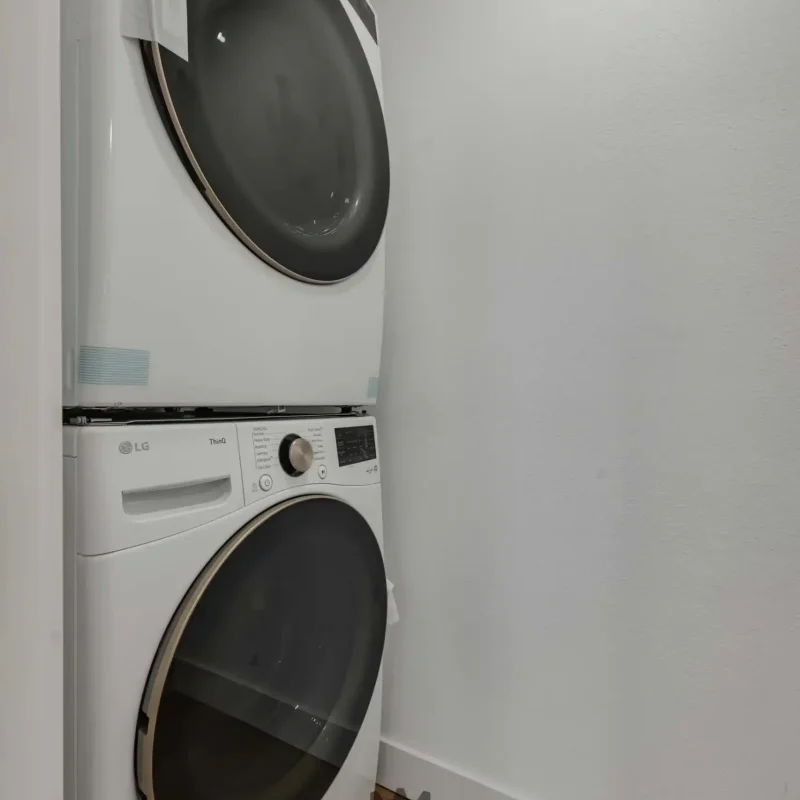 A compact stackable white washing machine and dryer unit set against a white wall.